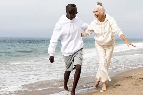 Older couple joyfully walking by the sea in casual clothing.