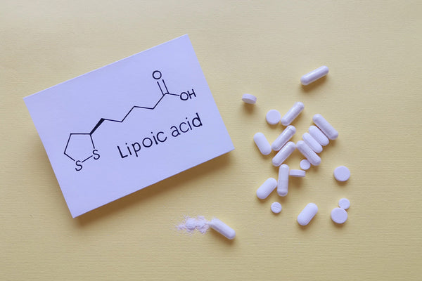 Chemical structure of lipoic acid with white pills on yellow background.
