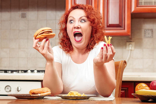 Woman joyfully holding a burger and fries in a kitchen.