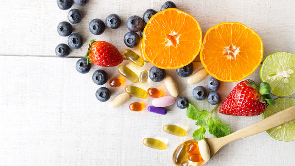 Fresh fruits and assorted supplements on a white wooden background.