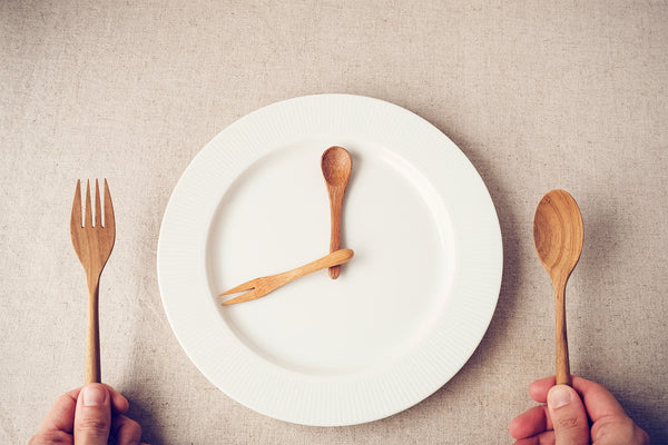 Wooden utensils on white plate resembling clock, representing meal time.
