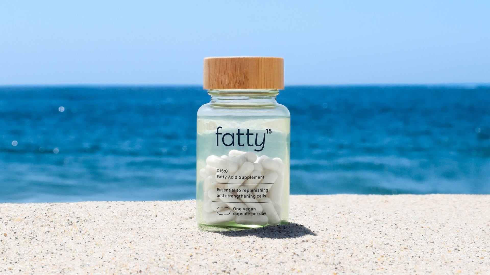 Fatty15's C15 supplement bottle on beach with ocean background.