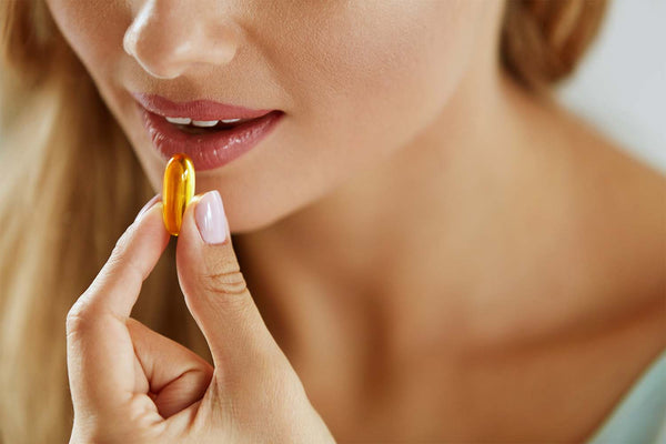 Woman holding a golden capsule near lips.