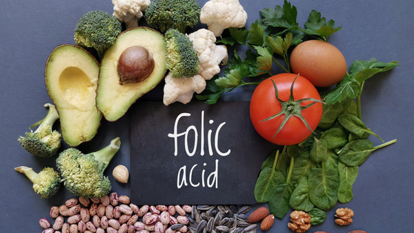 Foods rich in folic acid including avocado, tomato, broccoli, and spinach.