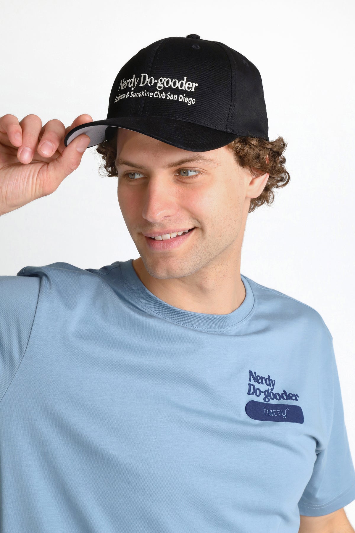 
                Man wearing a black cap and blue t-shirt, adjusting his cap with a smile.