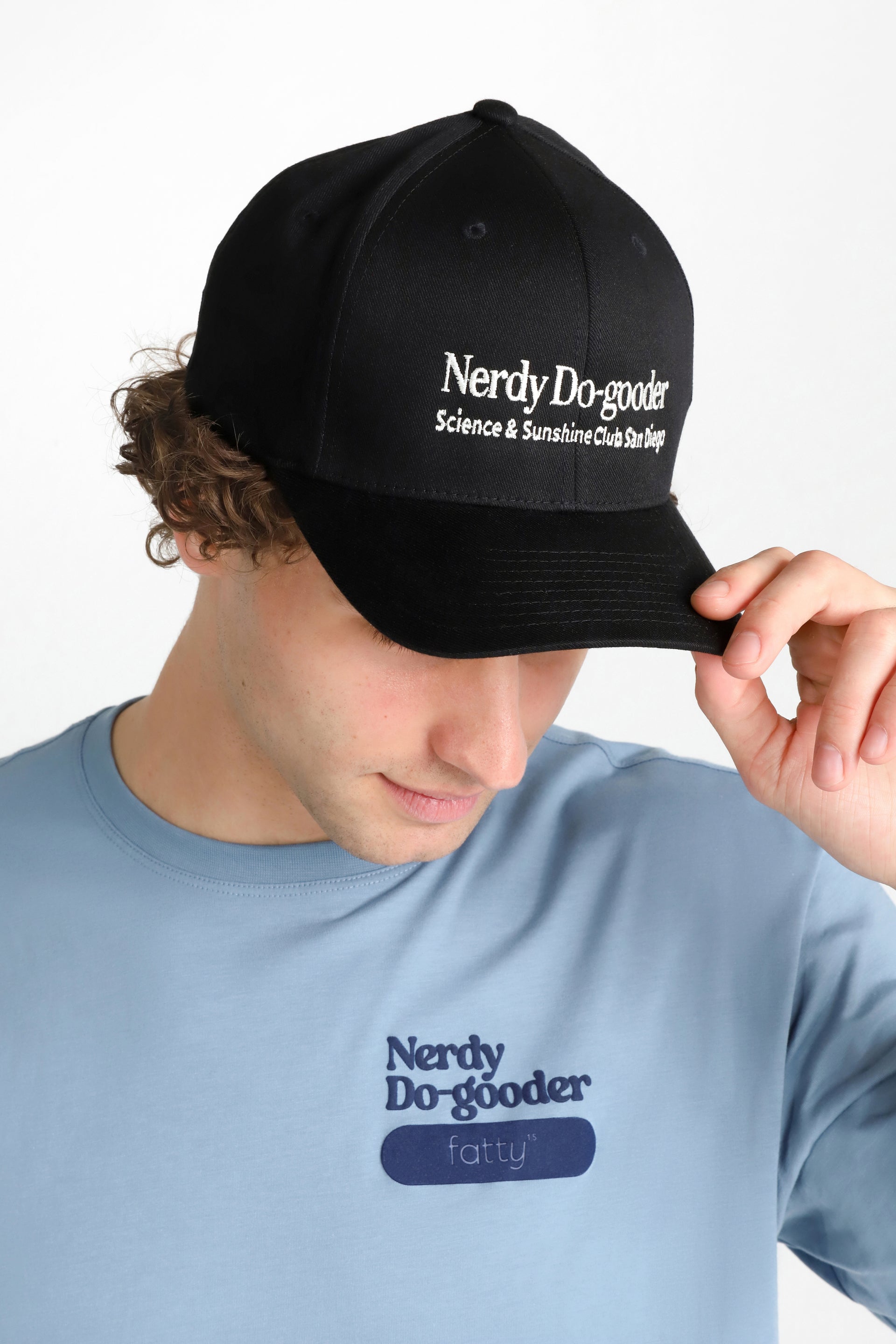 Man wearing a blue Nerdy Do-gooder T-shirt and black cap, looking down.