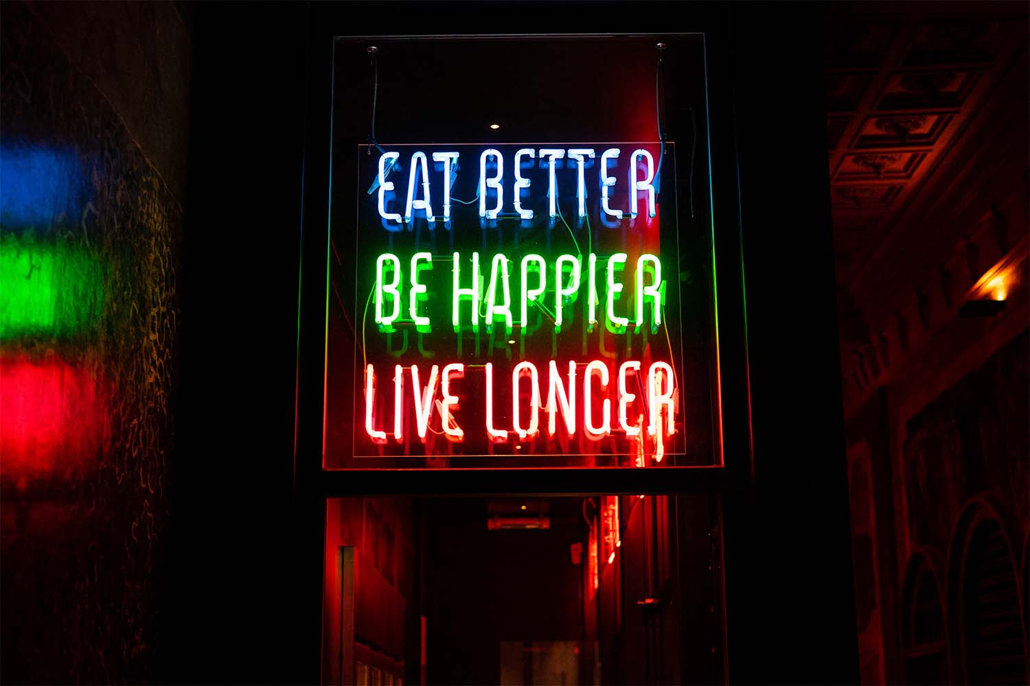 Neon sign with Eat Better, Be Happier, Live Longer in colorful lights.