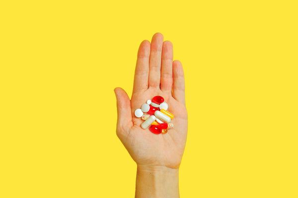 Hand holding assorted pills with yellow background.