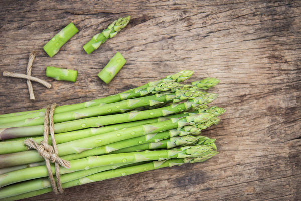 Fresh asparagus bundle on rustic wooden table.