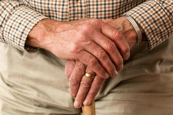 Elderly man's hands resting on a cane, wearing a checkered shirt.