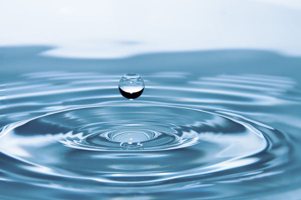Water droplet creating ripples on a calm blue surface.