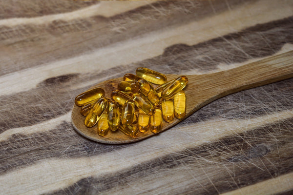 Wooden spoon with yellow oil capsules on a rustic table.