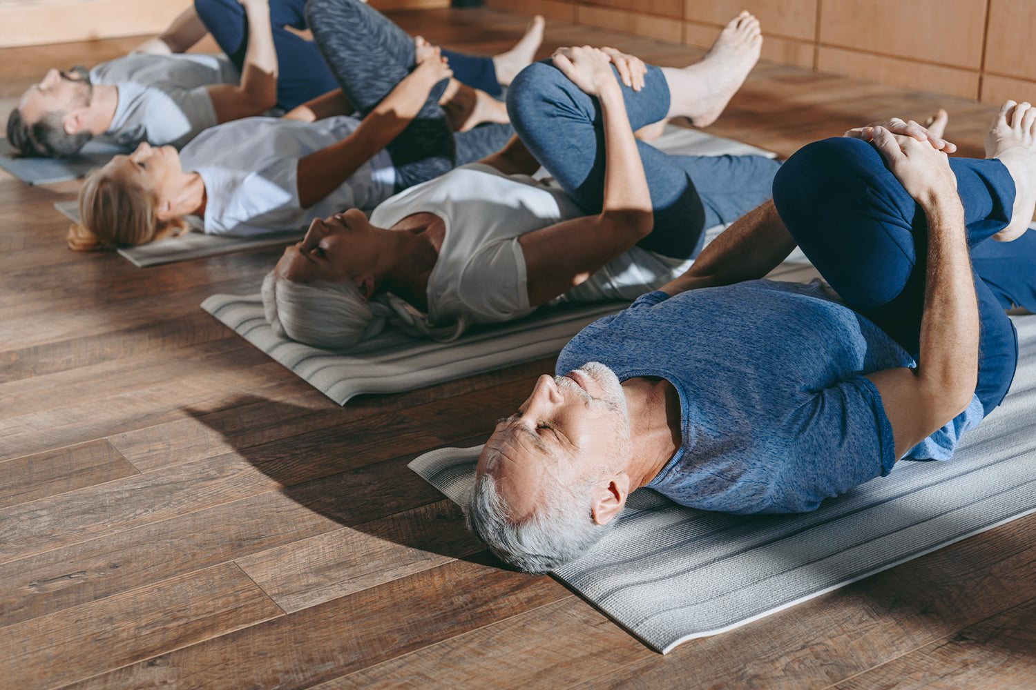 Elderly group doing yoga stretches on mats in a studio.