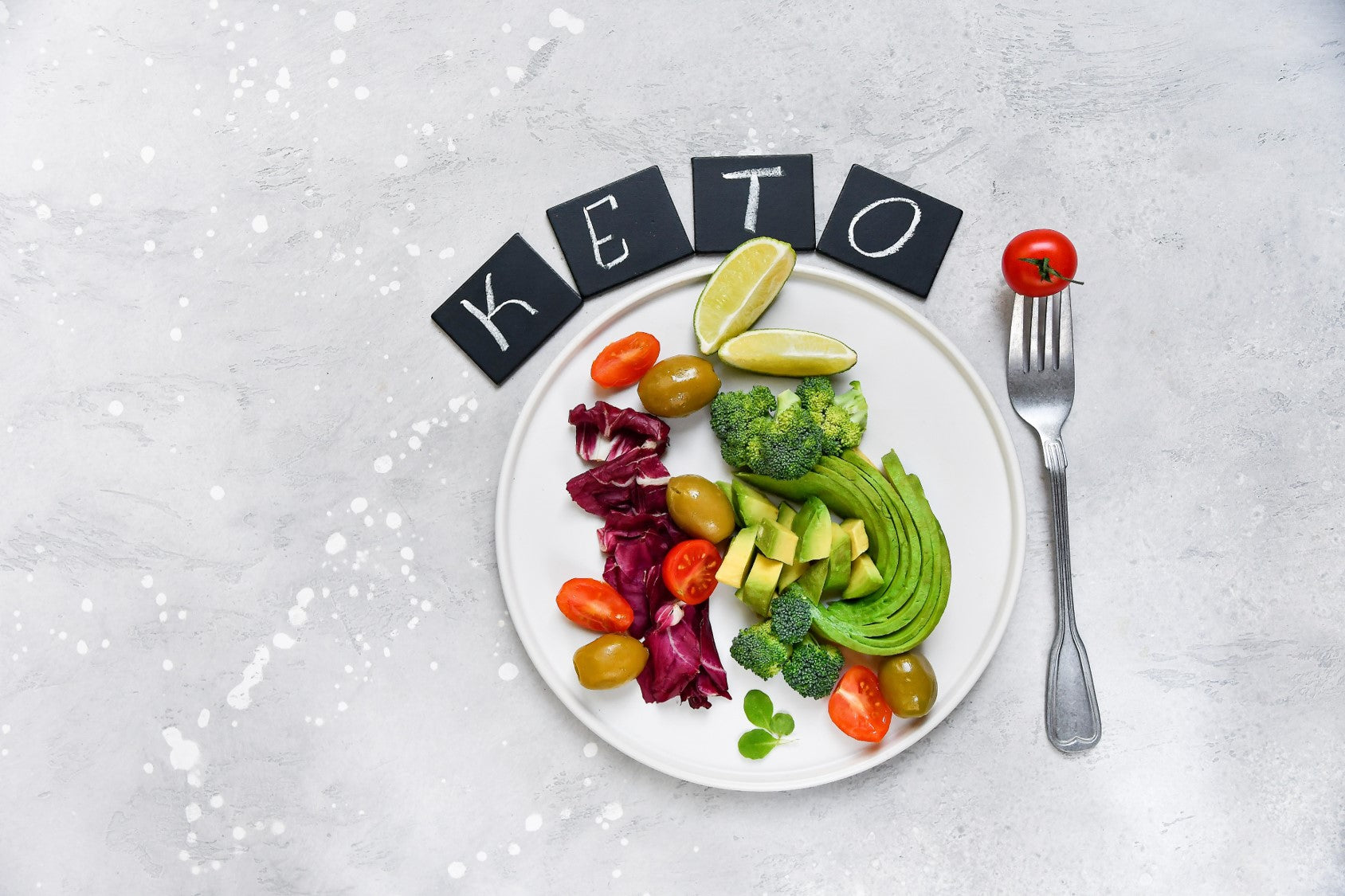 Healthy keto meal with avocado, olives, and lime on a white plate.