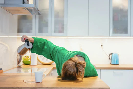 Person in green robe spilling coffee while half-asleep in kitchen.
