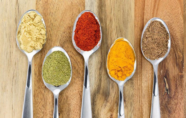 Five spoons of colorful spices on a wooden table.