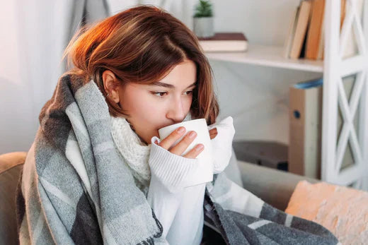 Woman wrapped in blanket enjoying a warm drink at home.